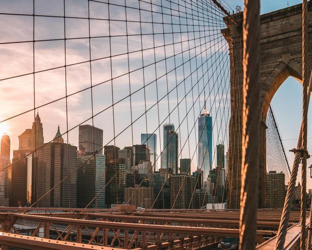 Close-up van de kabels en een pijler van de Brooklyn Bridge met de wolkenkrabbers van Manhattan op de achtergrond bij zonsondergang