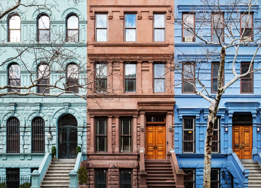 Drie naast elkaar staande rijtjeshuizen geschilderd in mintgroen, roodbruin en blauw met kale bomen ervoor in New York