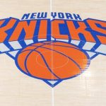 Close-up van het oranje en blauwe New York Knicks logo geschilderd op de houten vloer van de basketbalarena