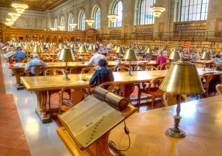 Bezoekers zitten te lezen aan houten tafels met bronzen lampen in de grote leeszaal van de New York Public Library