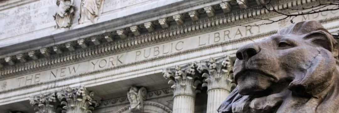 Close-up van een van de stenen leeuwenbeelden voor de ingang van de New York Public Library met de naam van het gebouw in steen gegraveerd