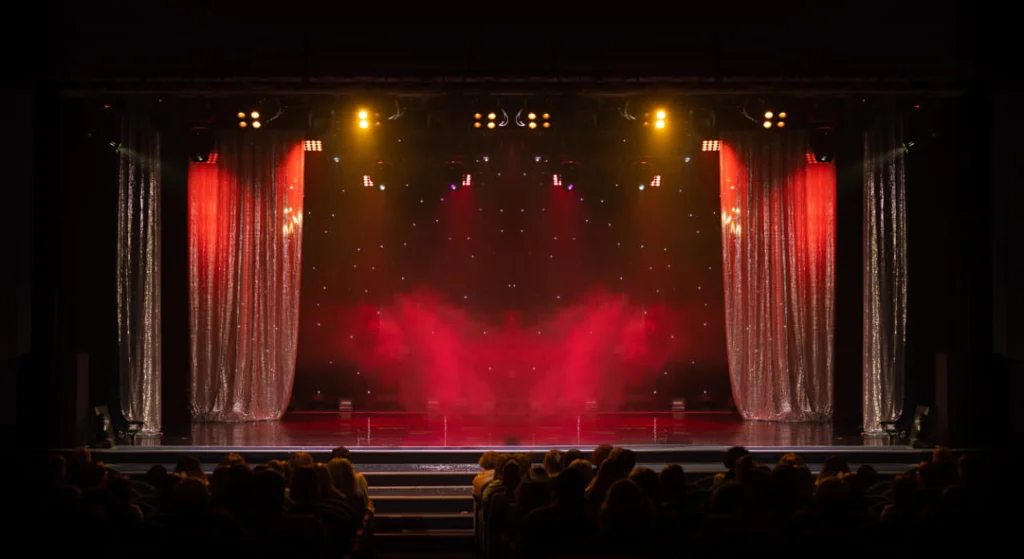 Verlaten theaterpodium met glinsterende rode gordijnen en gele spotlights boven een rij lege stoelen in een Broadway theater
