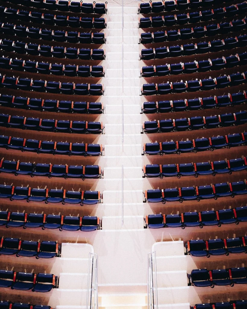 Luchtfoto van talloze rijen blauwe klapstoelen in een lege sportarena met een lichte middenpad ertussen