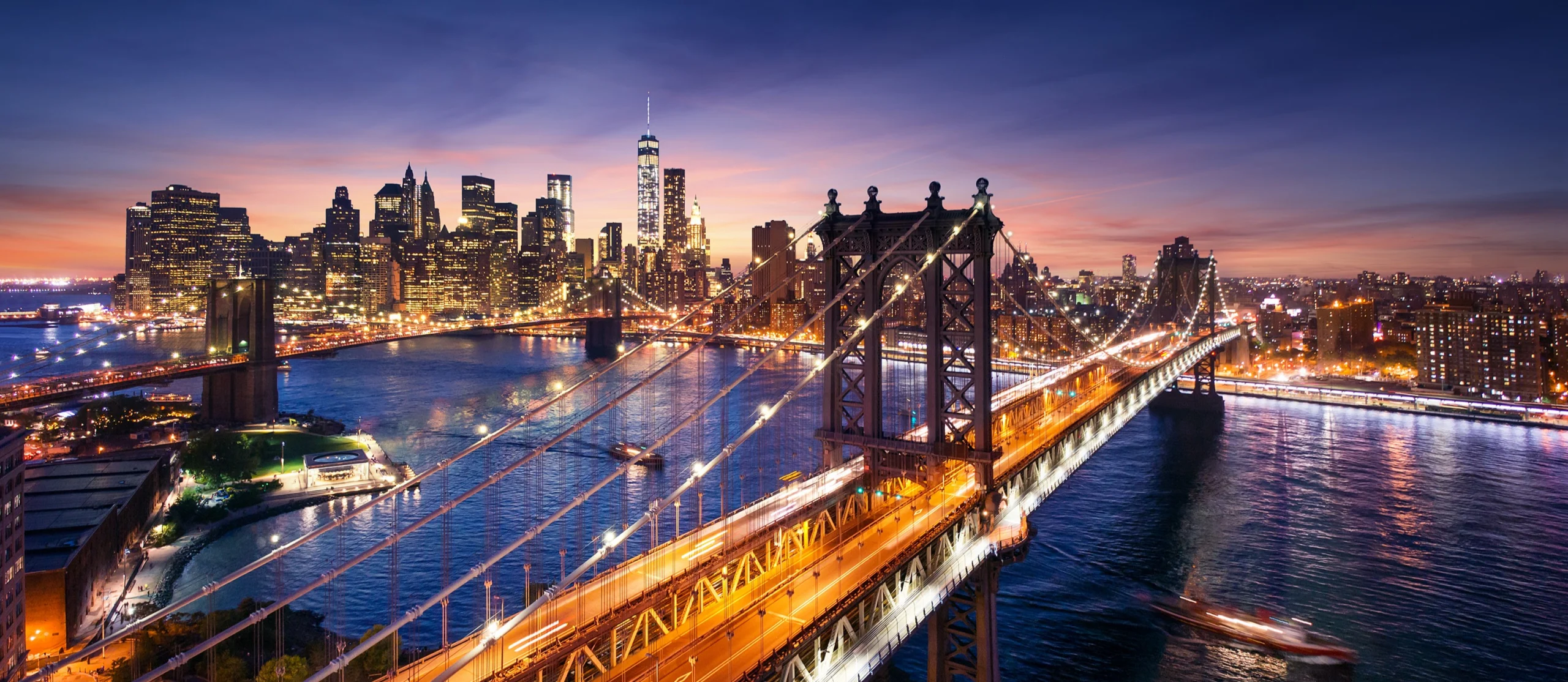 Luchtfoto van de verlichte Brooklyn Bridge en Manhattan Bridge met de skyline van Lower Manhattan op de achtergrond bij schemering