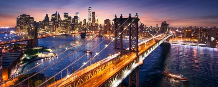 Luchtfoto van verlichte hangbruggen over de rivier met de skyline van Manhattan op de achtergrond bij schemering