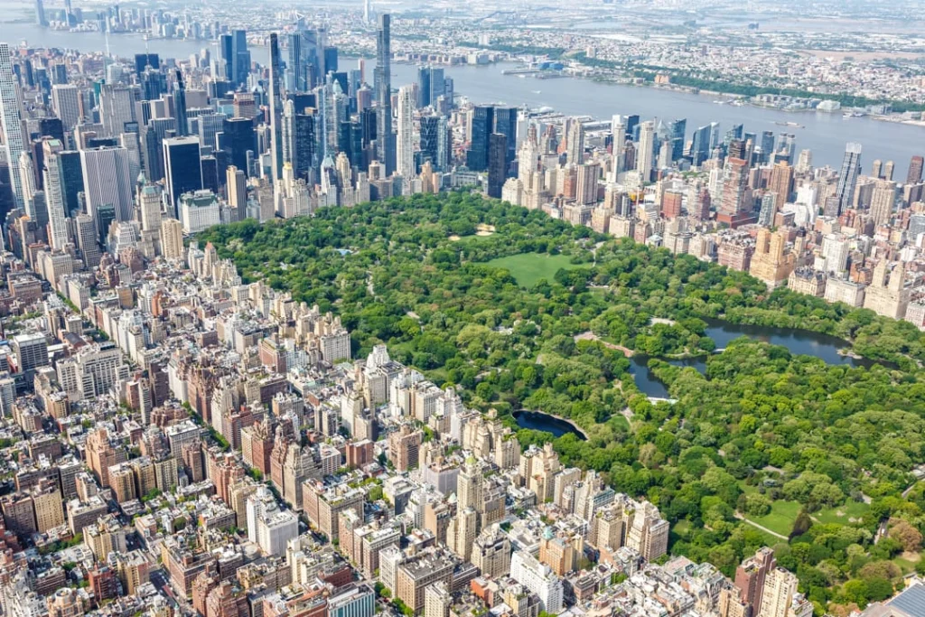 Luchtfoto van Central Park in New York, omringd door dichtbebouwde straten en hoge wolkenkrabbers met de rivier op de achtergrond