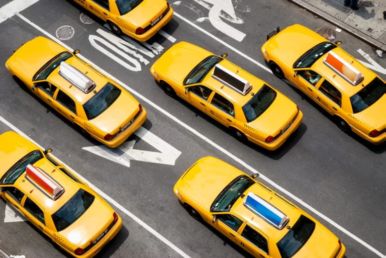 Luchtfoto van meerdere gele taxi's die naast elkaar rijden op een brede straat in New York, met witte rijstrepen op het asfalt