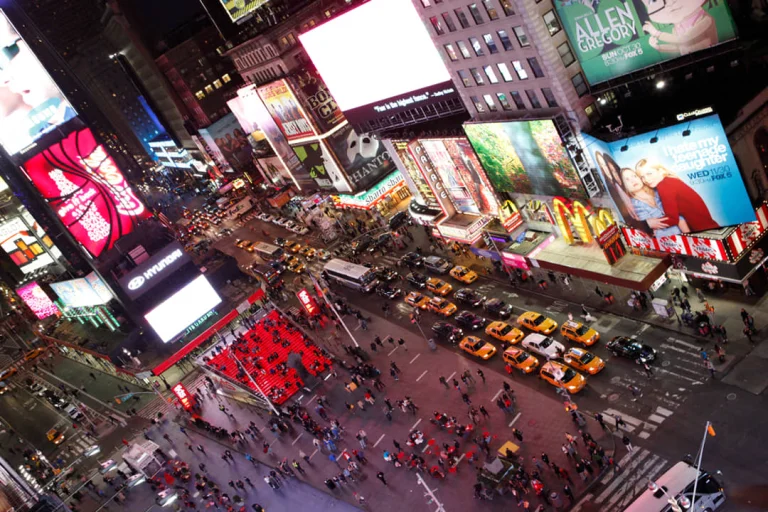 Bovenaanzicht van een drukke kruising op Times Square in de avond met gele taxi's, voetgangers en fel verlichte reclameborden