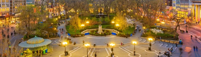Panoramisch avondzicht op Union Square in New York met verlichte wandelpaden, bomen, een kiosk en flanerende mensen