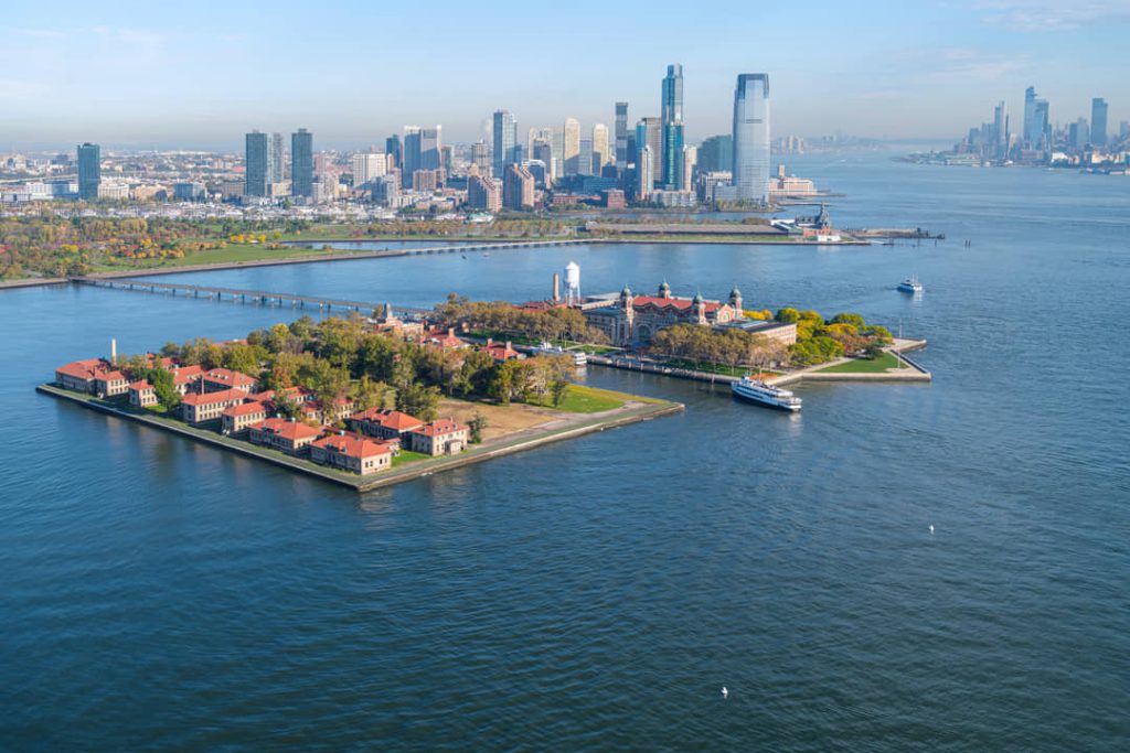 Luchtfoto van de gebouwen en aanlegsteiger van Ellis Island met het water van de baai en de skyline van New York in de verte