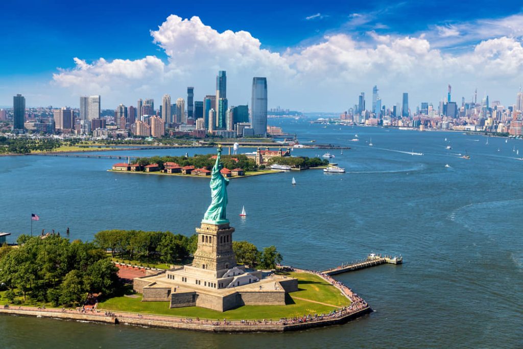 Luchtfoto van het Vrijheidsbeeld op zijn eiland omringd door blauw water met de skylines van Manhattan en Jersey City verderop