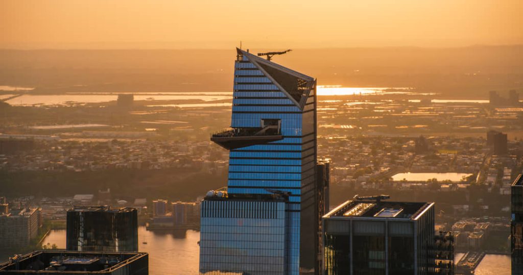 Luchtfoto bij zonsondergang van een puntige glazen wolkenkrabber met een uitstekend uitkijkplatform boven de stad New York