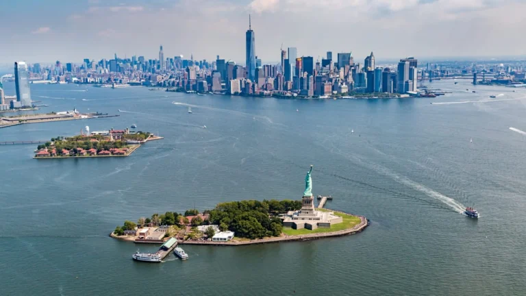 Luchtfoto van het Vrijheidsbeeld op zijn eigen eilandje met Ellis Island ernaast en de skyline van Manhattan in de verte