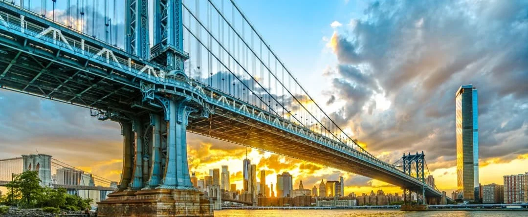 De Manhattan Bridge op de voorgrond en de Brooklyn Bridge op de achtergrond over de East River bij zonsondergang