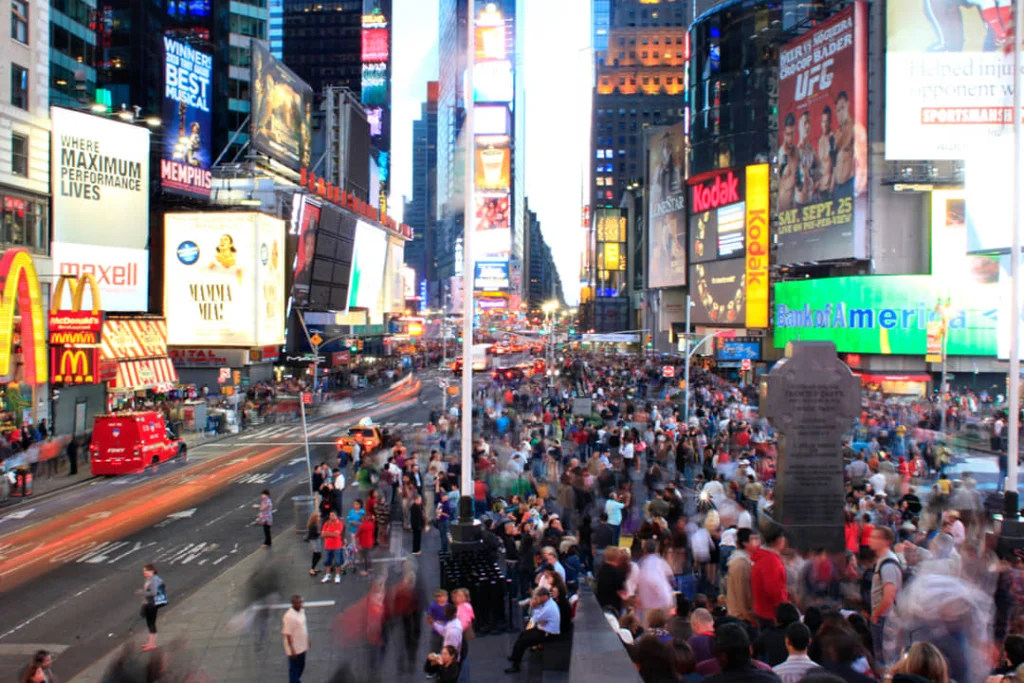 Volle voetgangerszone op Times Square met honderden mensen, een rode dubbeldekkerbus en fel verlichte reclameborden bij schemering