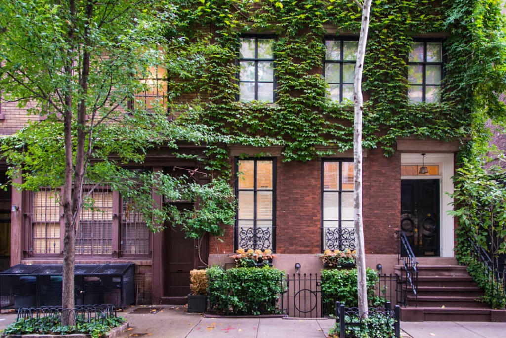 Bakstenen herenhuis in Greenwich Village met de volledige gevel begroeid met groene klimop en een bloeiende voortuin