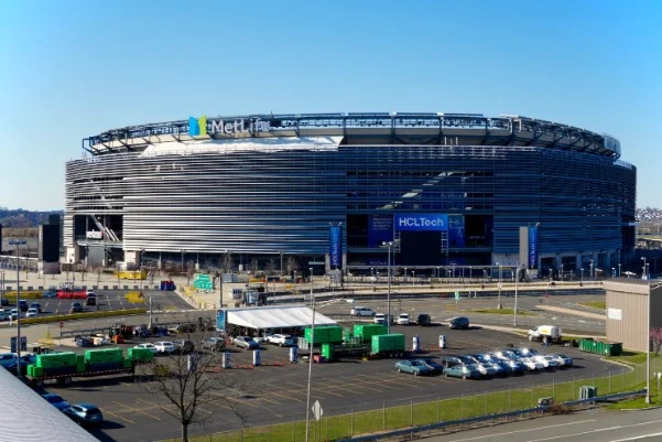 Luchtfoto van het ovale MetLife Stadium met een grote parkeerplaats ervoor onder een strakblauwe lucht