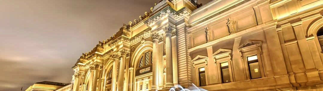 Verlichte klassieke gevel met zuilen van het Metropolitan Museum of Art tegen een donkere avondlucht in New York