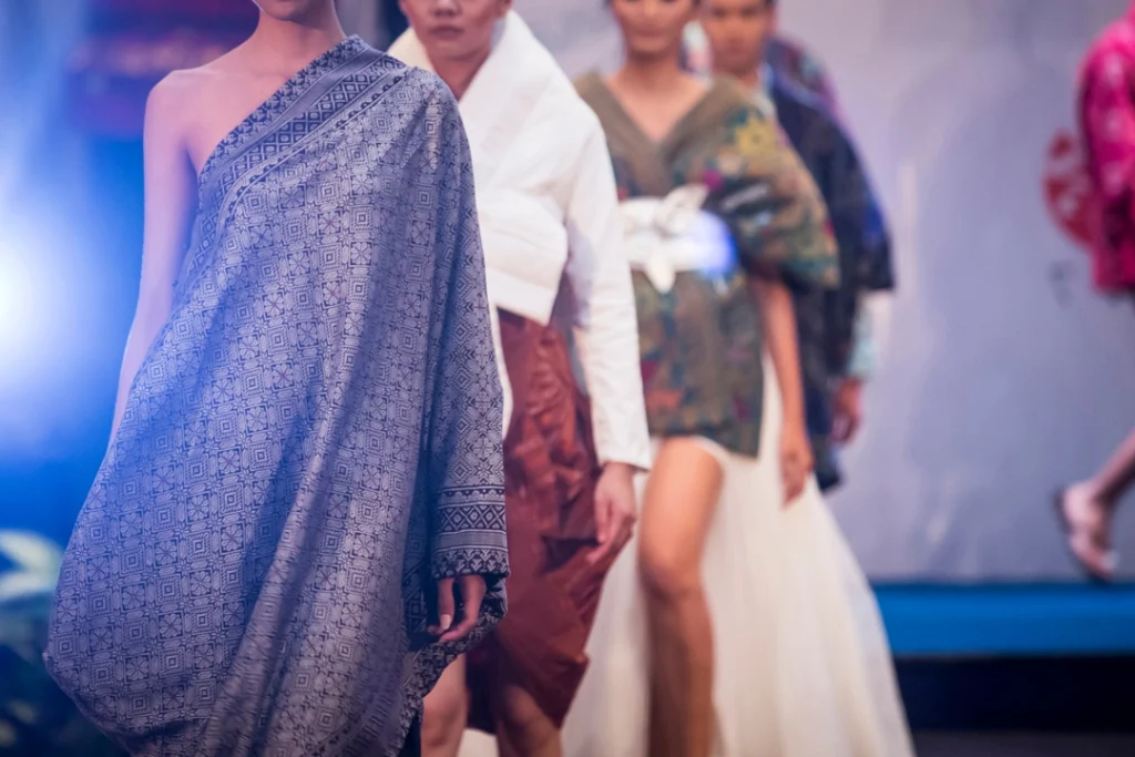 Modellen in gedrapeerde traditionele stoffen met patronen lopen achter elkaar over de catwalk