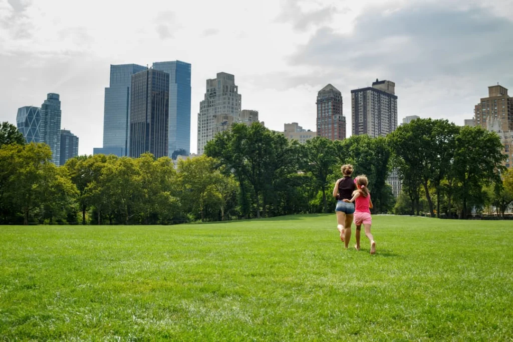 Moeder en dochter rennen hand in hand over een groen grasveld in Central Park met wolkenkrabbers aan de horizon