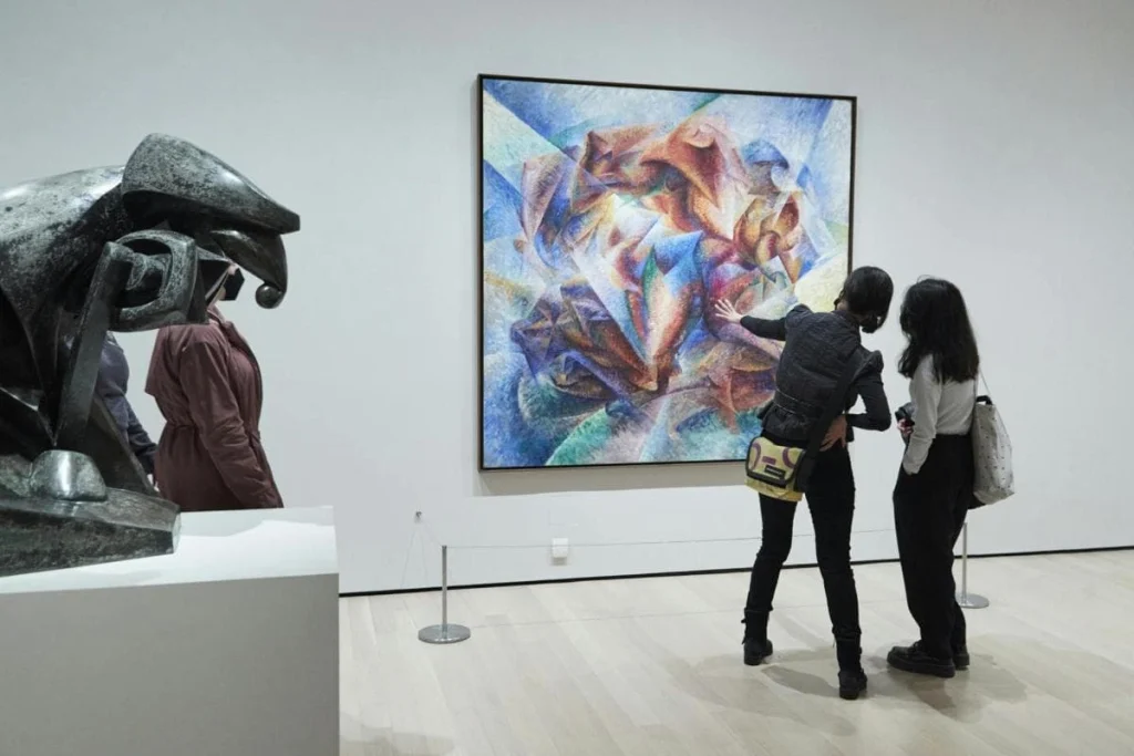 Twee bezoekers bekijken een abstract futuristisch schilderij in een galerie van het Museum of Modern Art in New York, met een bronzen sculptuur op de voorgrond