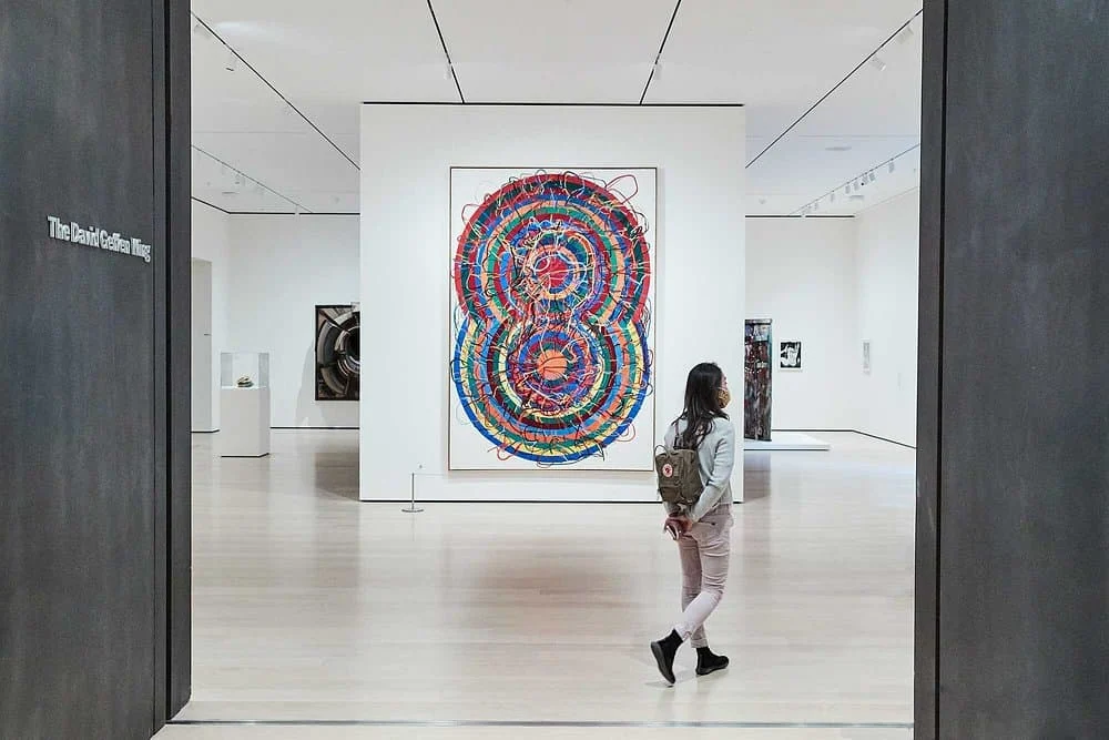 Bezoeker staat voor een groot kleurrijk cirkelvormig kunstwerk in een galerie van het Museum of Modern Art in New York