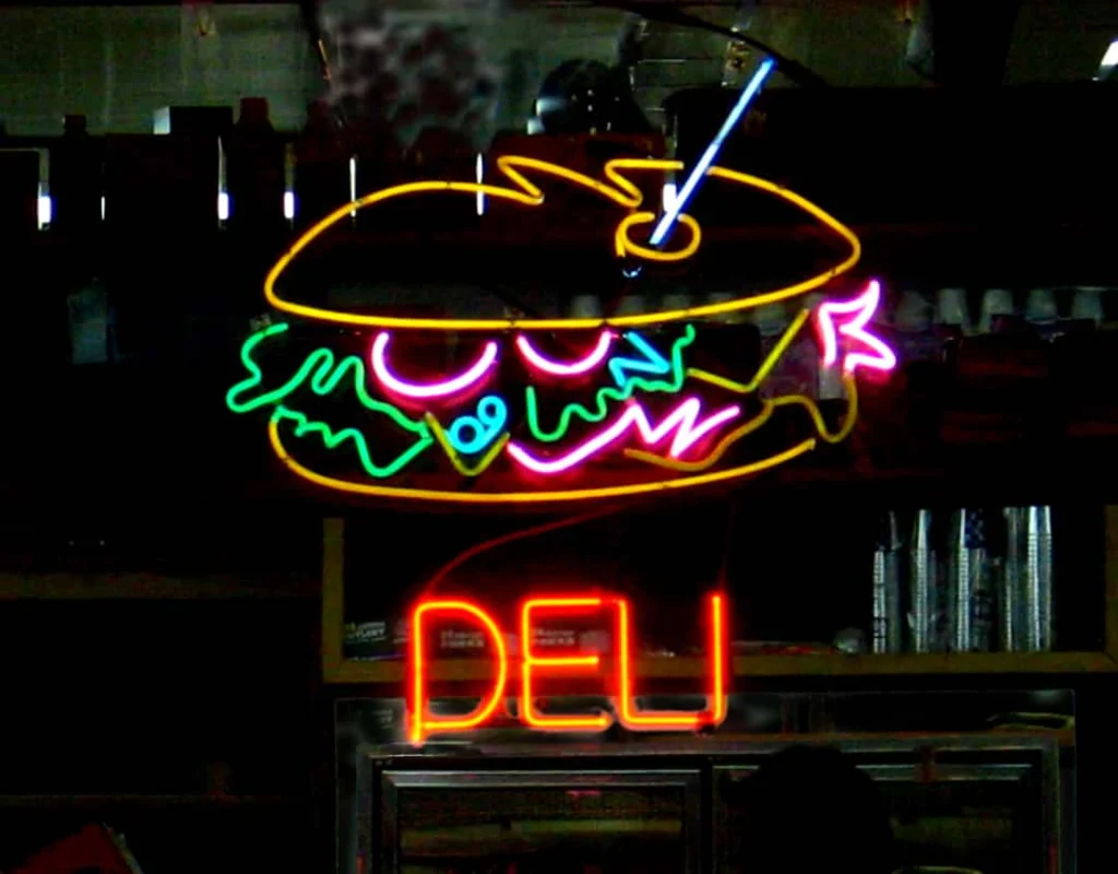 Kleurrijk neonbord met een broodje en de tekst deli hangt in het donkere interieur van een delicatessenzaak