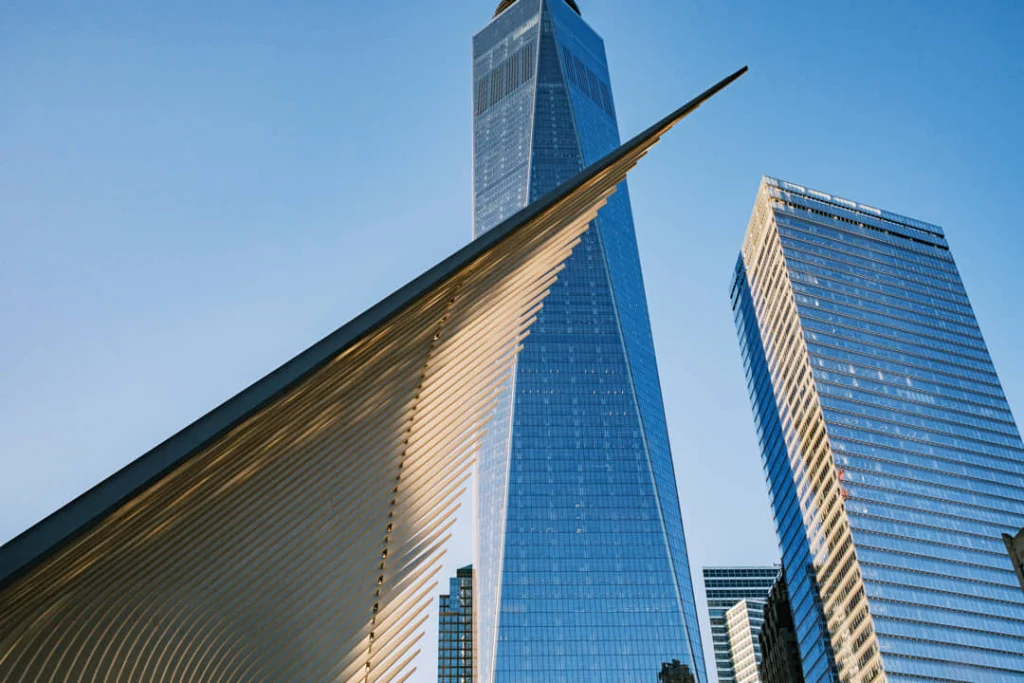 Vleugelvormig wit dak van het Oculus treinstation onder een blauwe lucht met de toren van One World Trade Center erachter