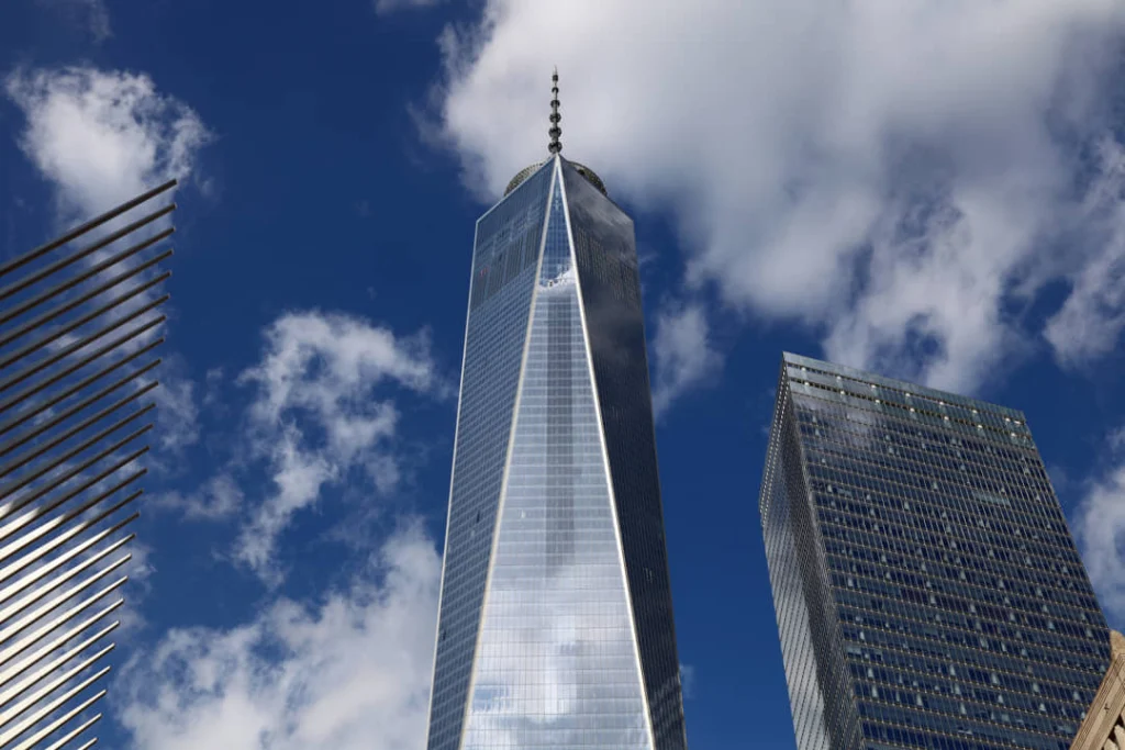 Laag standpunt op de glazen top van One World Trade Center tegen een bewolkte blauwe lucht met de Oculus ernaast