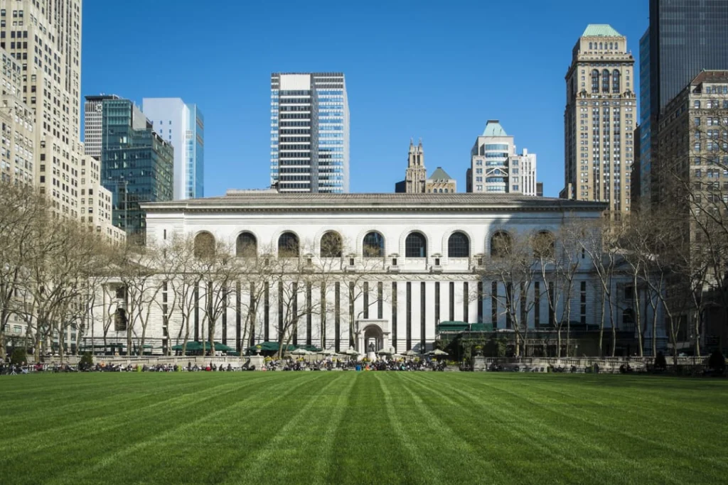 Klassiek witte gevel van de New York Public Library met kale bomen en een groen grasveld op de voorgrond