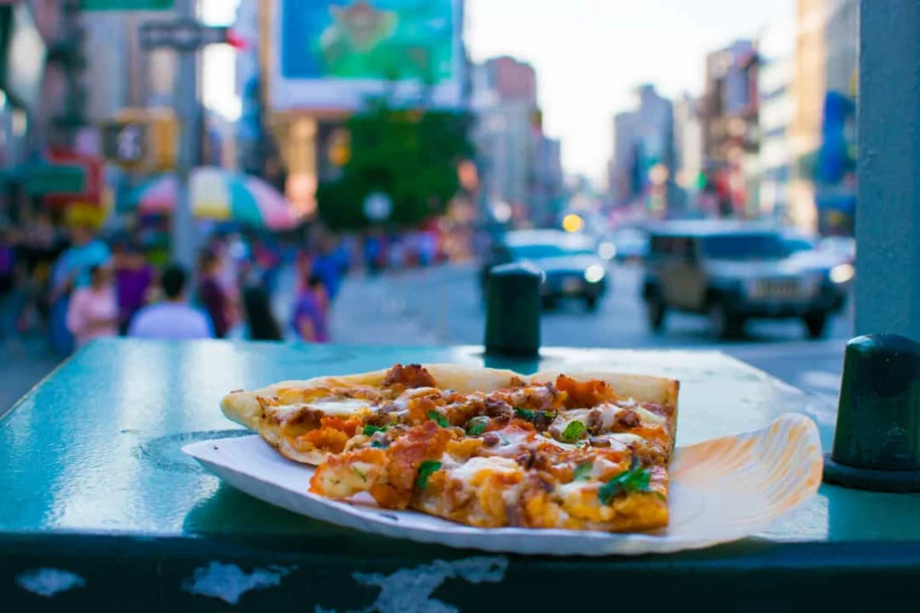 Twee punten pizza op een papieren bordje liggen op een richel met een wazige drukke straat op de achtergrond
