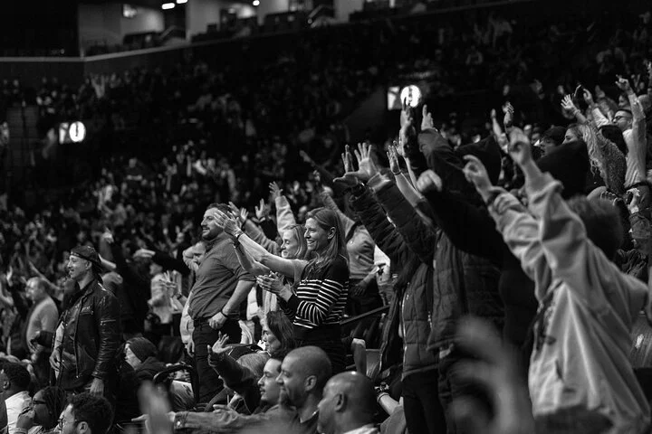 Zwart wit foto van toeschouwers die met opgeheven armen juichen tijdens een basketbalwedstrijd op de tribune