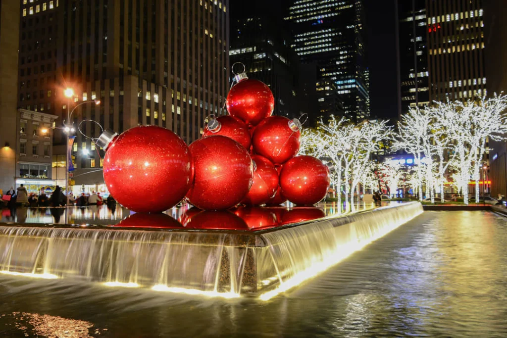 Enorme rode kerstballen op een verlichte fontein tussen wolkenkrabbers met verlichte bomen in de achtergrond in New York