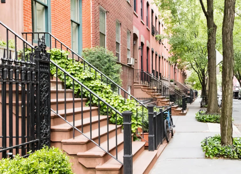 Rij bakstenen herenhuizen in Greenwich Village met stoepen begroeid met klimop en een fiets tegen het hek