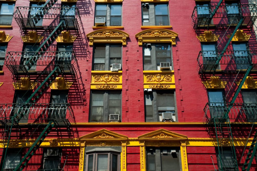 Felrode gevel van een appartementengebouw met gouden sierlijsten boven de ramen en zwarte brandtrappen ervoor in Chinatown