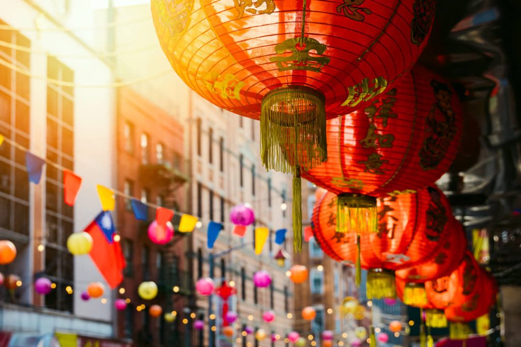 Close-up van hangende rode Chinese lantaarns met gouden opschriften en kleurrijke vlaggetjes boven een straat in Chinatown