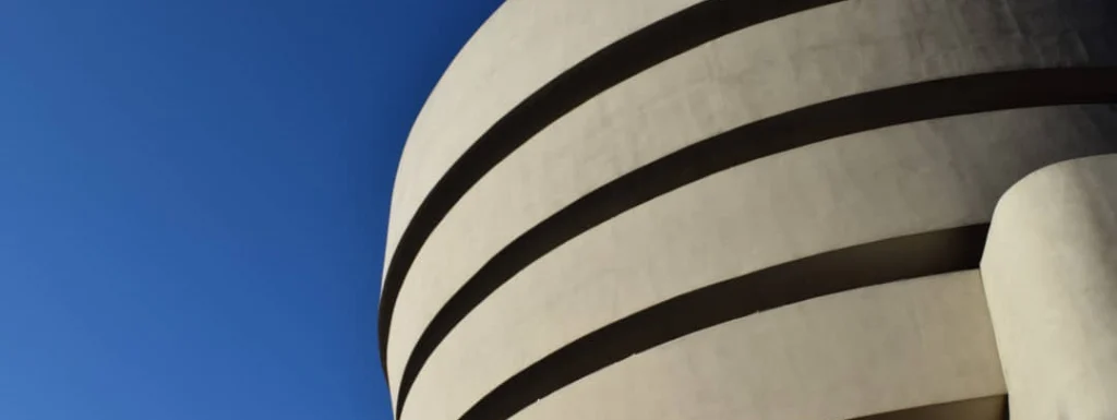 Kenmerkende gebogen betonnen gevel van het Guggenheim Museum met horizontale banden tegen een strakblauwe hemel
