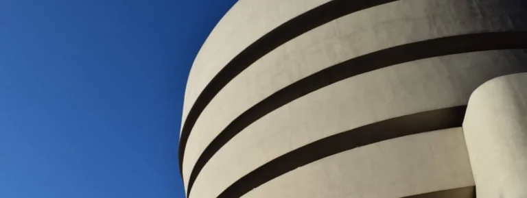 Kenmerkende gebogen betonnen gevel van het Guggenheim Museum met horizontale banden tegen een strakblauwe hemel
