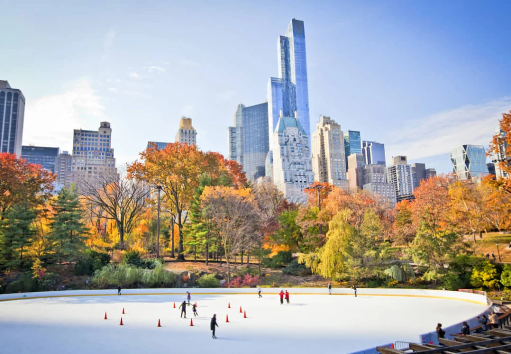 Schaatsers rijden rondjes op een buitenbaan in Central Park terwijl herfstbomen en wolkenkrabbers de achtergrond vormen
