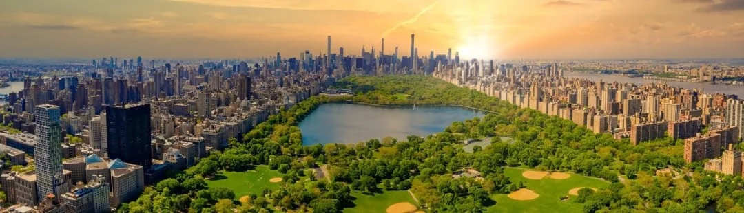 Tientallen schaatsers op een buitenijsbaan in Central Park omringd door herfstbladeren en de skyline van Manhattan op de achtergrond