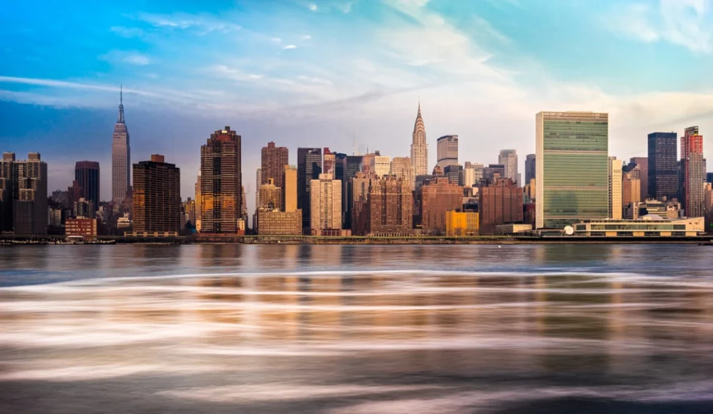 Skyline van Manhattan over het water bij zonsondergang met de Empire State Building, de Chrysler Building en het VN gebouw