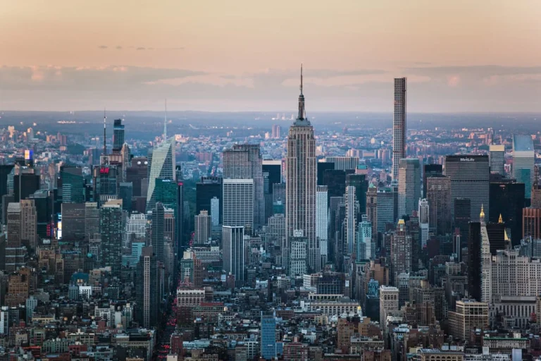 Wolkenkrabbers van Manhattan gehuld in een roze en oranje avondlucht met het verlichte Empire State Building duidelijk zichtbaar boven de stad