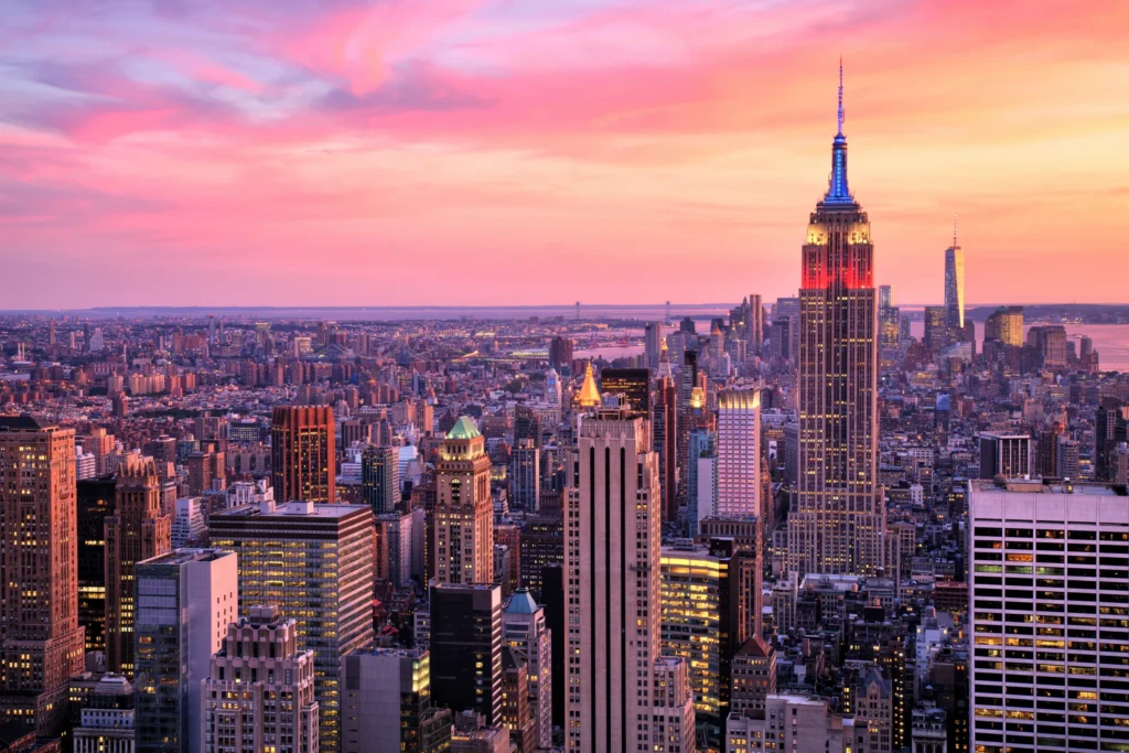 Uitzicht over de skyline van Manhattan in New York met de verlichte Empire State Building onder een roze en oranje zonsonderganghemel