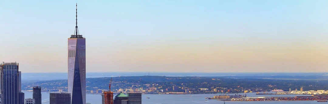 Uitzicht op de skyline van Lower Manhattan met de spits van One World Trade Center boven de wolkenkrabbers bij zonsondergang