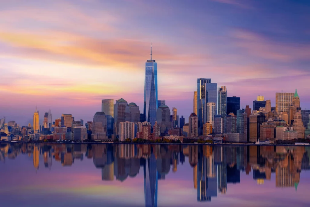 Wolkenkrabbers van Lower Manhattan met de One World Trade Center toren kleuren roze en oranje bij zonsondergang met een spiegelend wateroppervlak