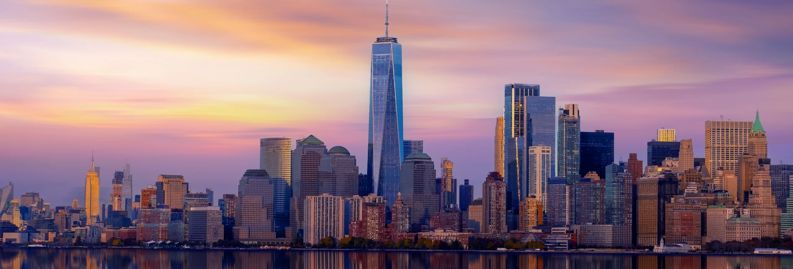 Panorama van de wolkenkrabbers van Lower Manhattan met de One World Trade Center toren die roze en paars kleuren bij zonsondergang