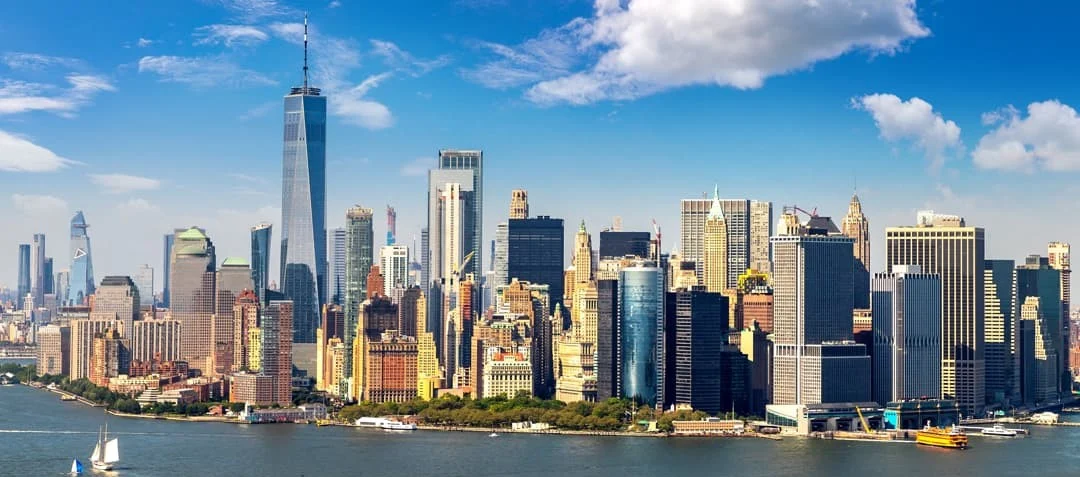 Panoramisch zicht op de skyline van Lower Manhattan vanaf het water, met One World Trade Center en een zeilboot