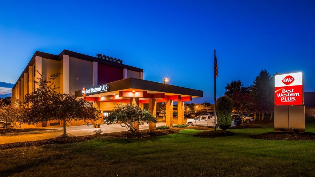 Verlichte gevel van een Best Western Plus hotel met luifel en parkeerplaats bij het vallen van de avond