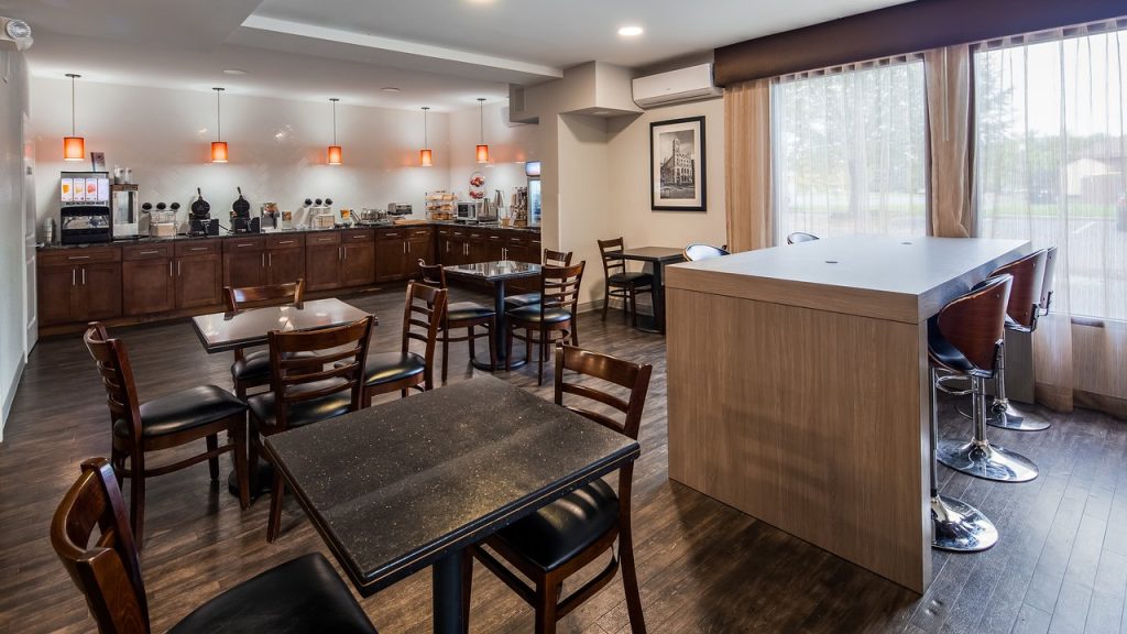 Ontbijtzaal met houten tafels en stoelen, een buffet met wafelijzers en een raam met uitzicht op groen