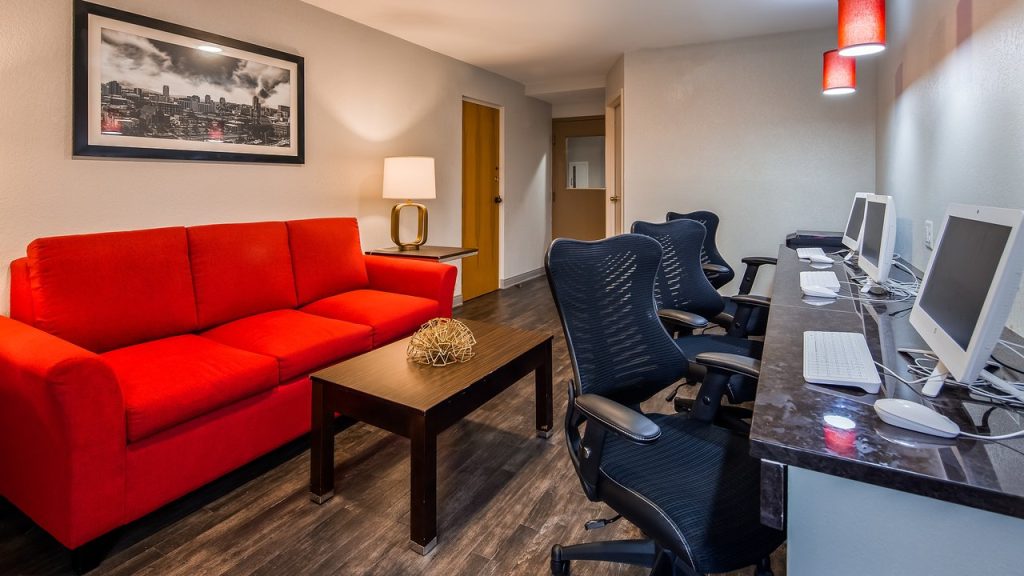Rode bank en fauteuils rond een salontafel naast een rij computers op een bureau in een hotellounge
